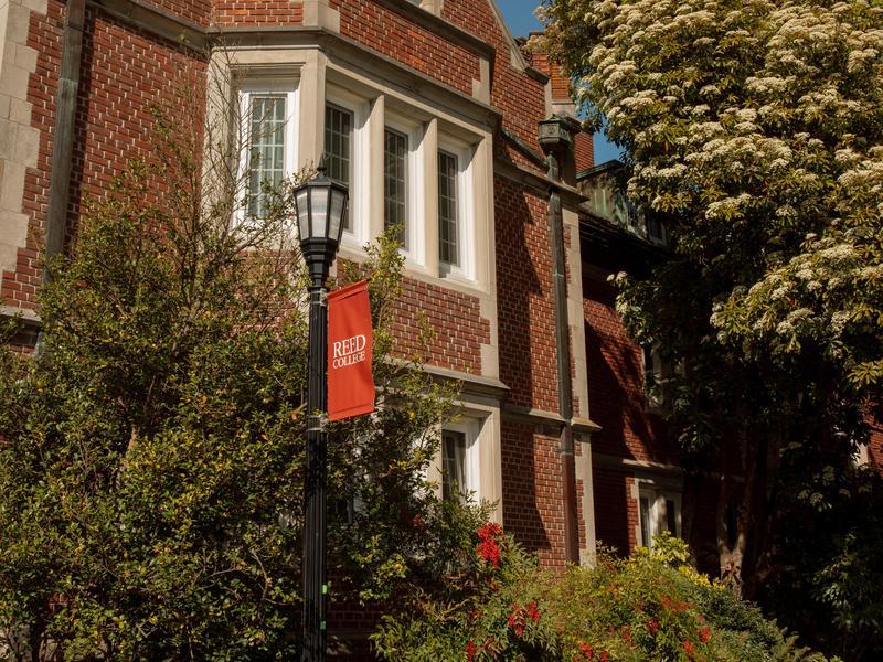 A red sign with white lettering and a griffin says Reed College rises above a brick building and trees