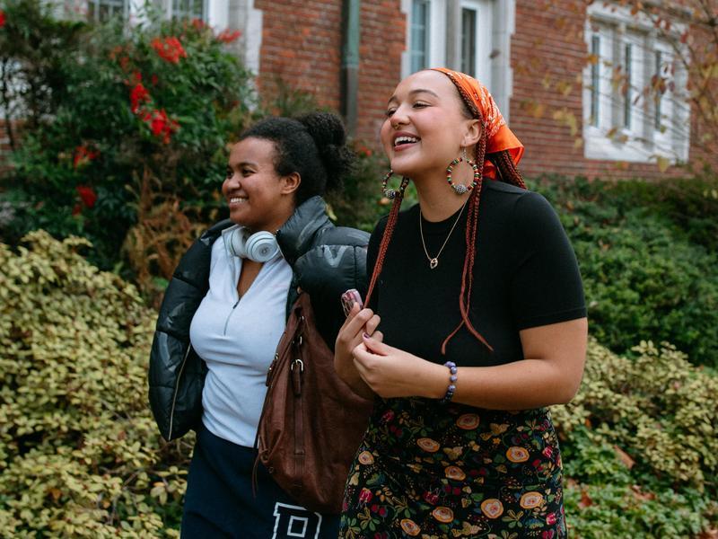 Two students smile while walking on campus.