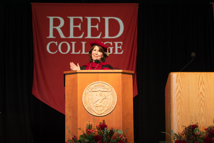 President of Reed College standing behind at a podium at commencement clapping.