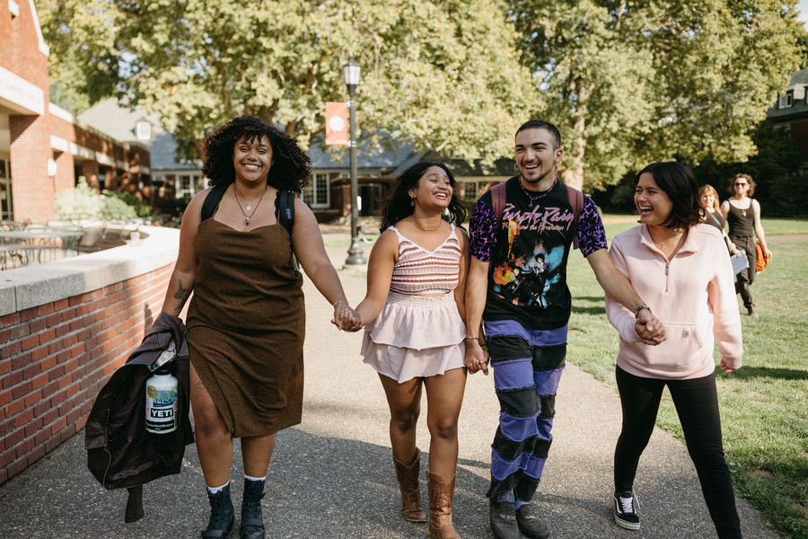 Four students are walking hand in hand, while smiling. 