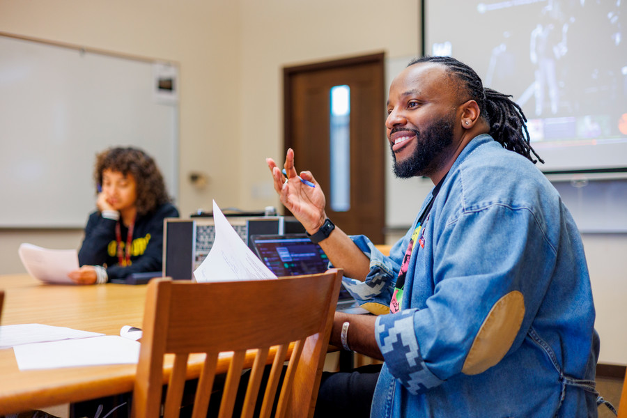 Dr K sitting at a table with students, facing them and talking.