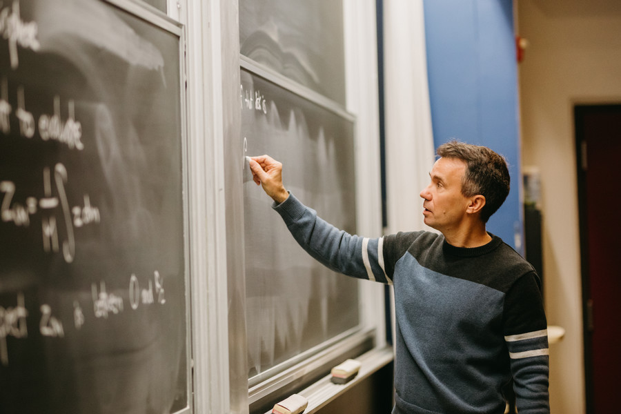 Professor standing in front of a chalk board writing a math equation.