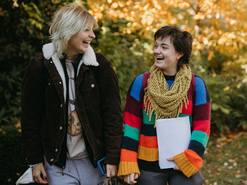 Two students are standing next to each other, looking at one another with wide smiles.