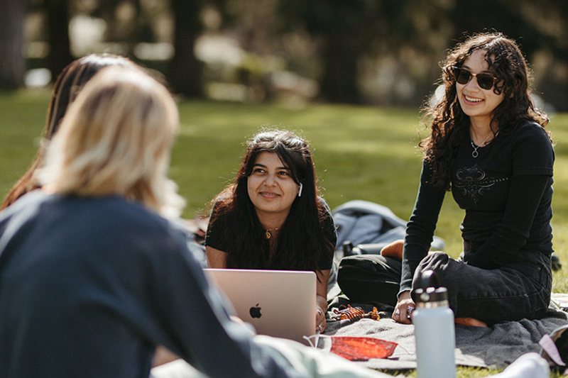 Students using their laptops on the Great Lawn and laughing.