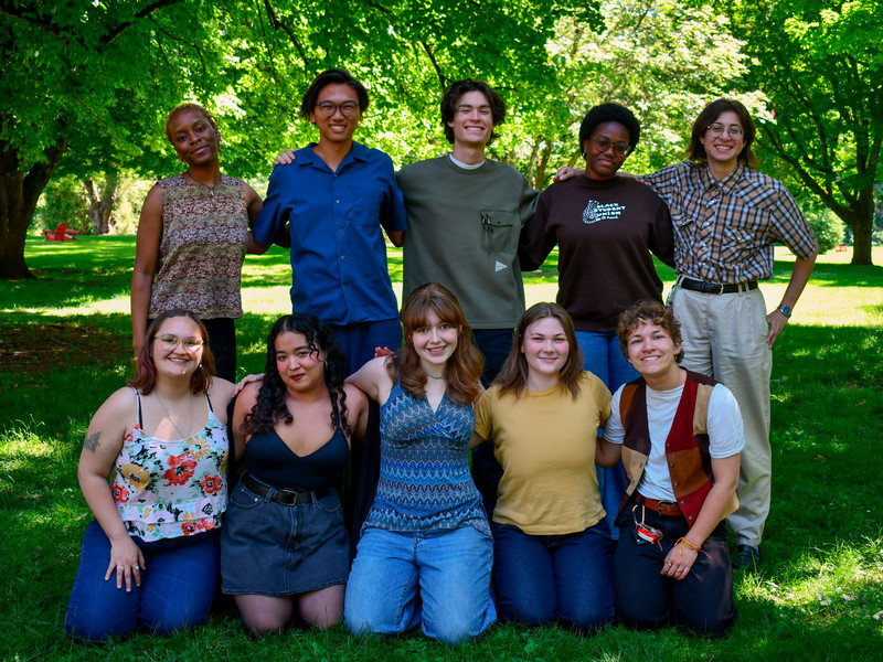 A group of current Reed students are posing for a group photo under the trees and smiling.