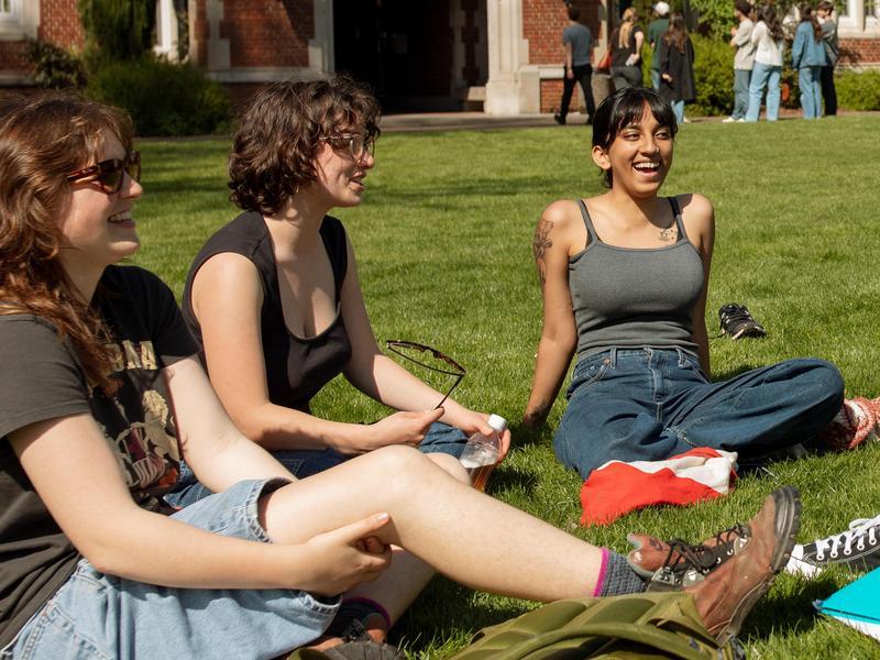 Three students relaxing and smiling on the Great Lawn.
