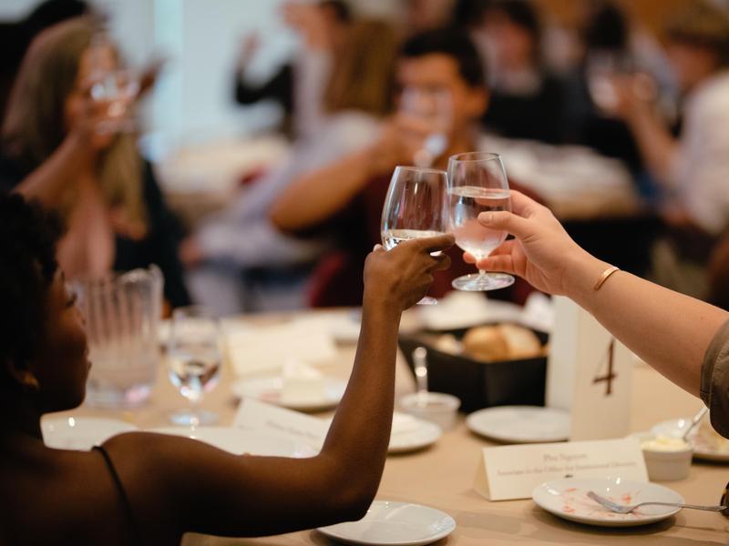 A table of dinner guests raise glasses of water and clink them together during a toast.