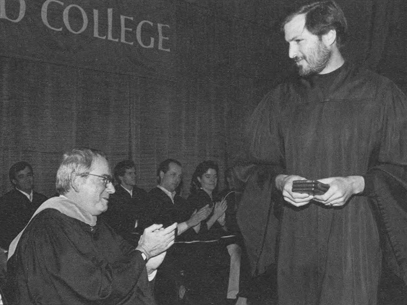 Steve Jobs in a black commencement gown on stage at the 1991 Reed College convocation ceremony, accepting the Vollum Award, being applauded by faculty members also wearing commencement gowns
