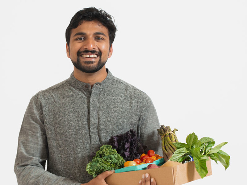 A portrait photo of Aditya Gadkari, who is wearing a kurta and holding a box of fresh fruits and vegetables