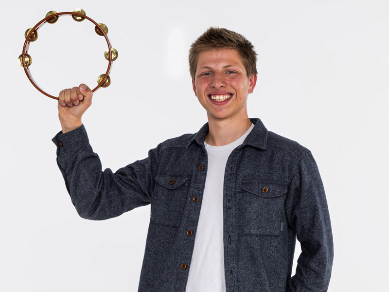 A portrait photo of Andrey Marsavin who has a tambourine raised in his right hand