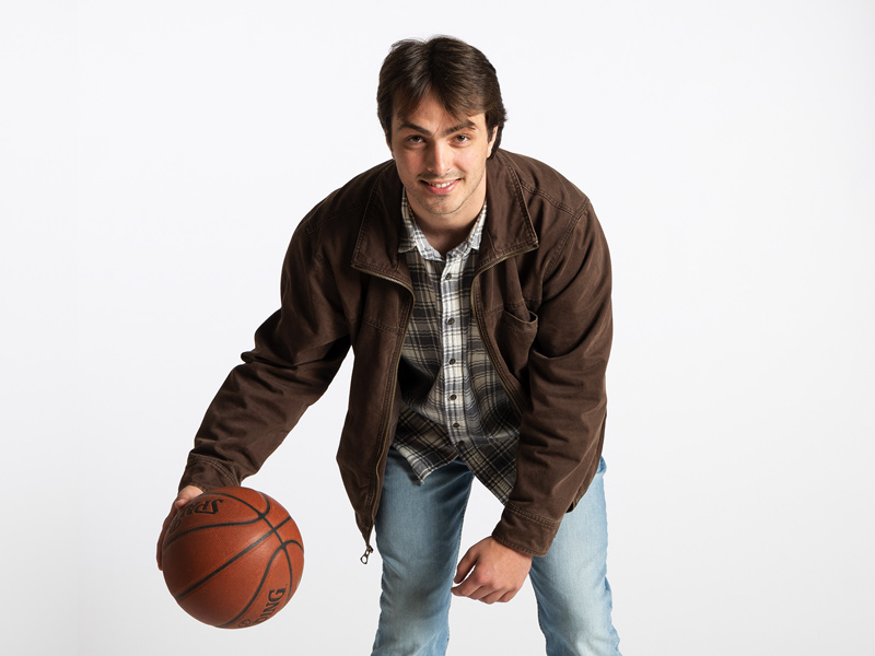 A portrait photo of Caden Corontzos who is hunched forward and dribbling a basketball