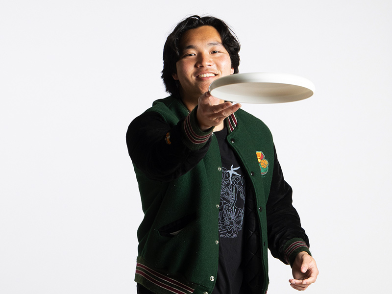 A portrait photo of Joshua Park who is fliging a frisbee at the viewer