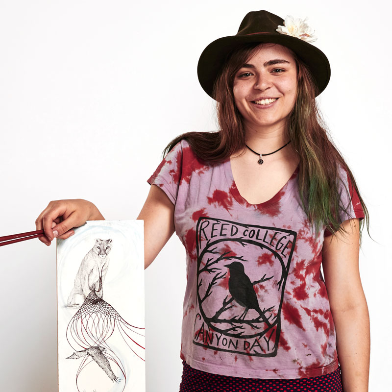 A portrait photo of Leila Pyle, who displays a sketch that shows symbols from the Pacific Northwest and holds two paintbrushes
