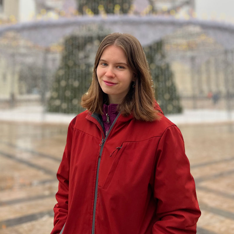 A portrait photo of Reedie Vilma Kodyte wearing a red jacket and standing in front of a large Christmas tree in Lithuania