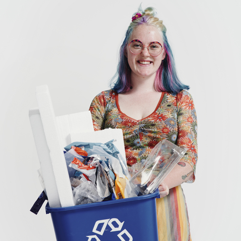 A portrait photo of Hayden Hendersen, who holds a blue recycling bin full of different materials