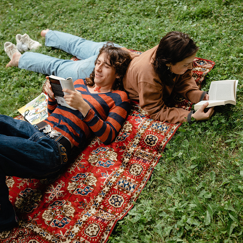 Two Reed students lie on a blanket on the grass reading.