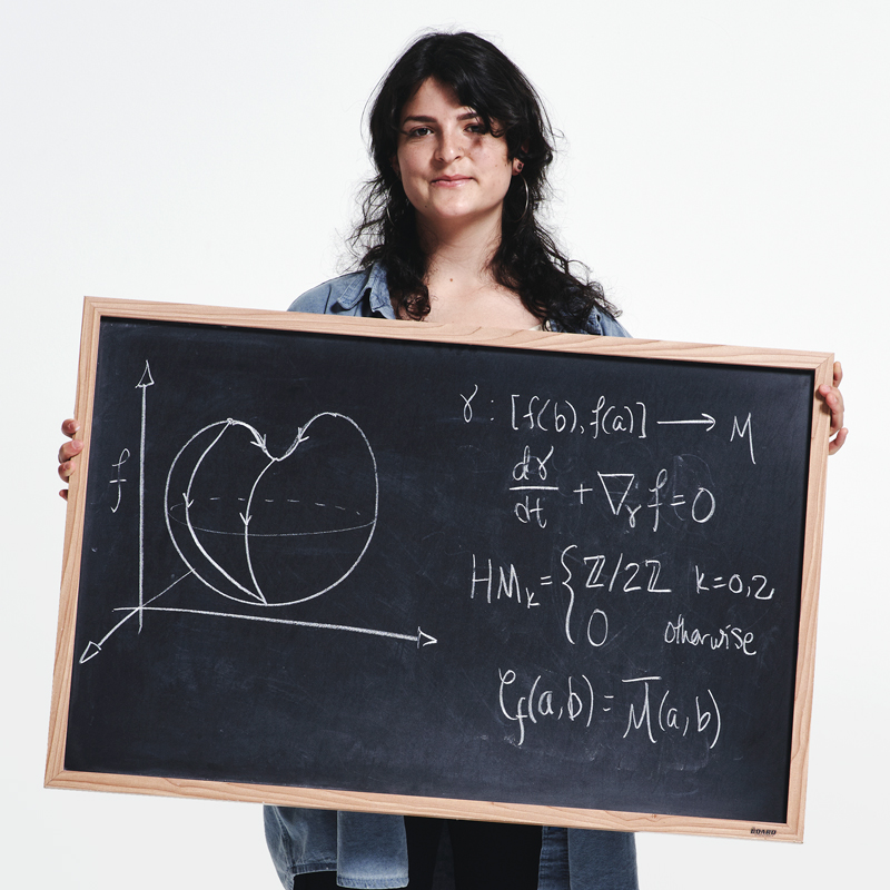A portrait photo of Maxine Elena Calle, who holds up a chalkboard with a mathematical equation