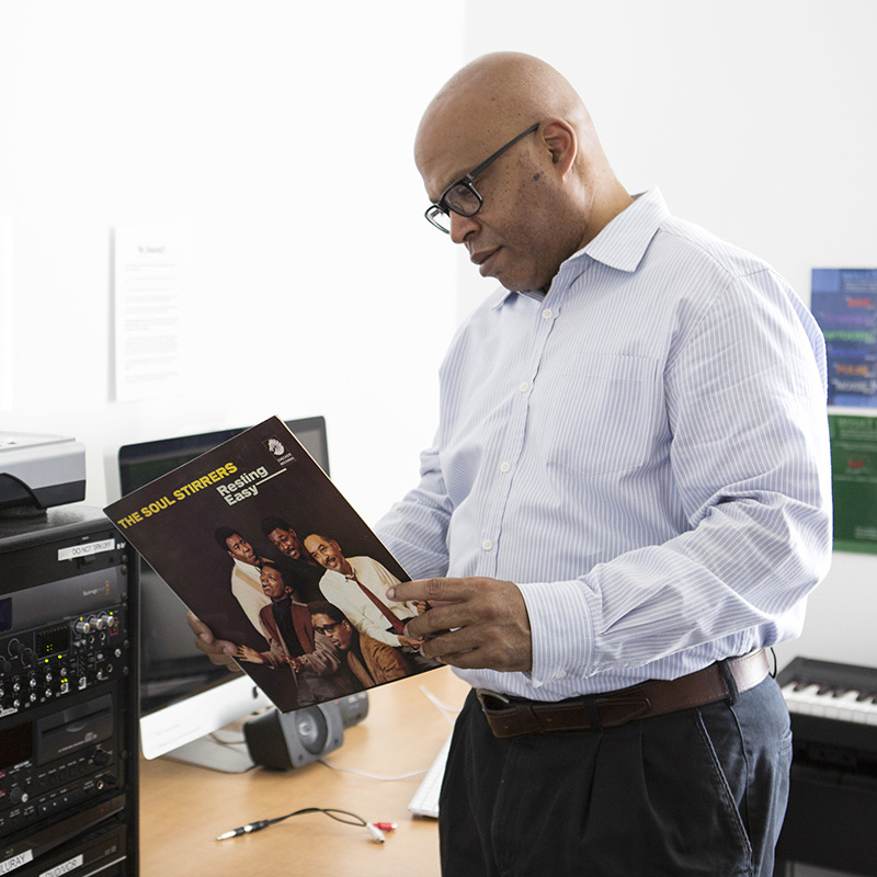 Mark Burford, professor of music, stands next to a record player. He is looking at an album by The Soul Stirrers.