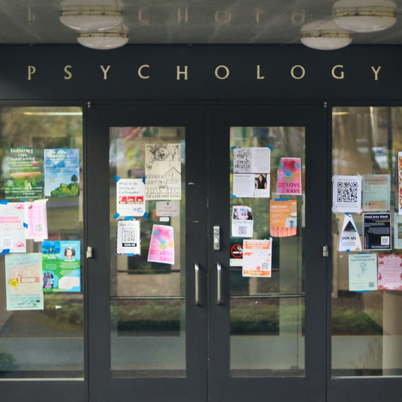 The glass double doors leading to the psychology building are covered with colorful flyers