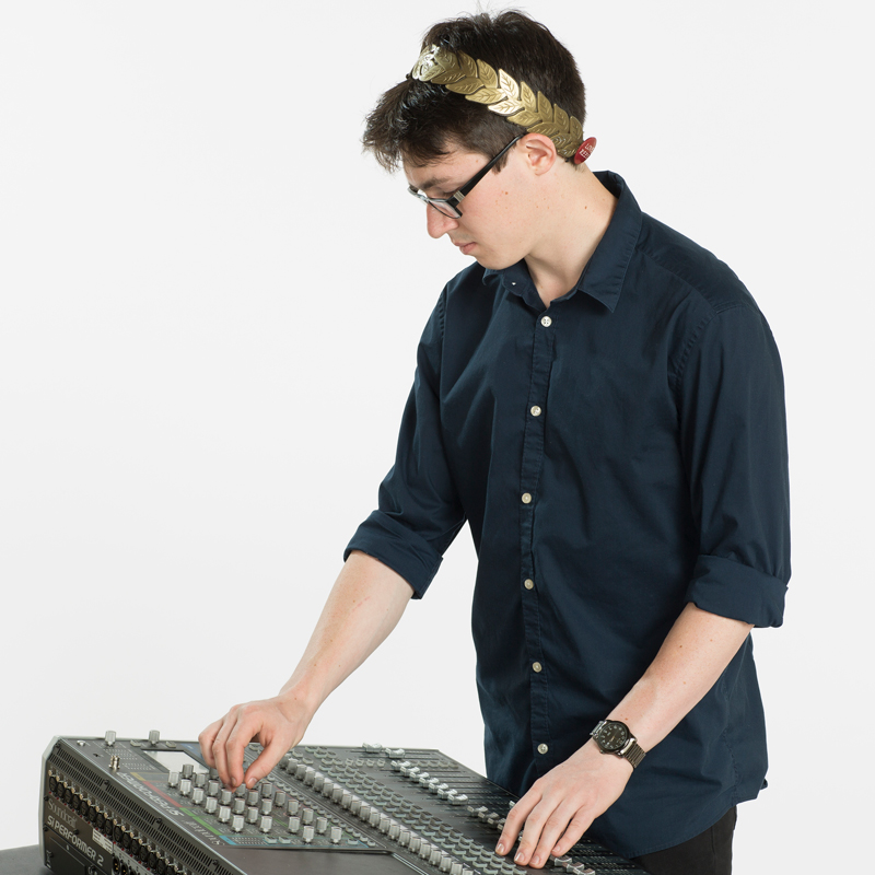 A portrait photo of Alexander Swann, who is wearing his Reed laurels and adjusting a mixing board