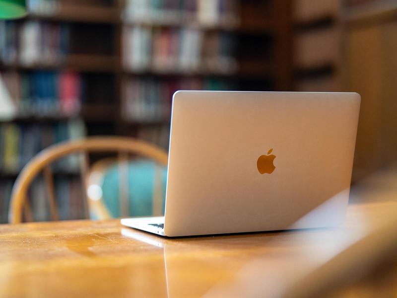 An open laptop sitting on a wooden table in a library.