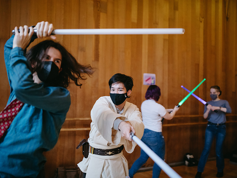 Reed College students wear masks and swinging lightsabers in different directions during the Paideia program