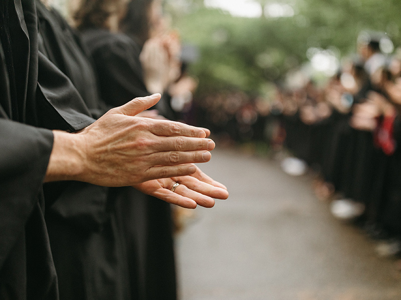 A pair of hands applauds graduates at a commencement ceremony