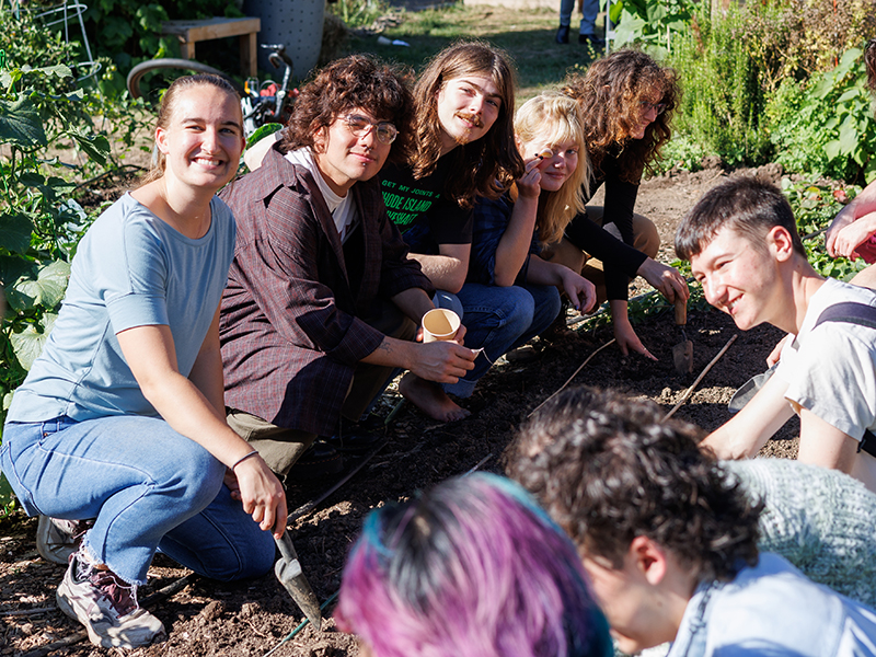 Two rows of students pose for a photo while planting in the Reed garden.