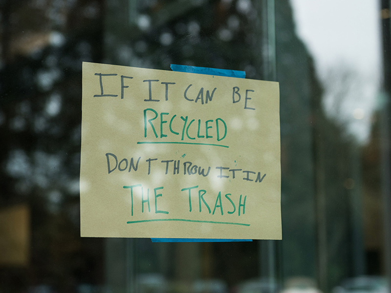A handwritten sign taped to a window that reads: "If it can be recycled, don't throw it in the trash."