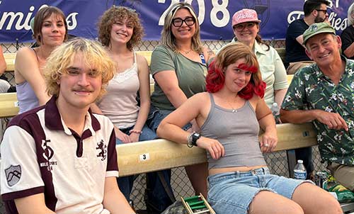 Seven lab folks posing in the stands of a sporting event