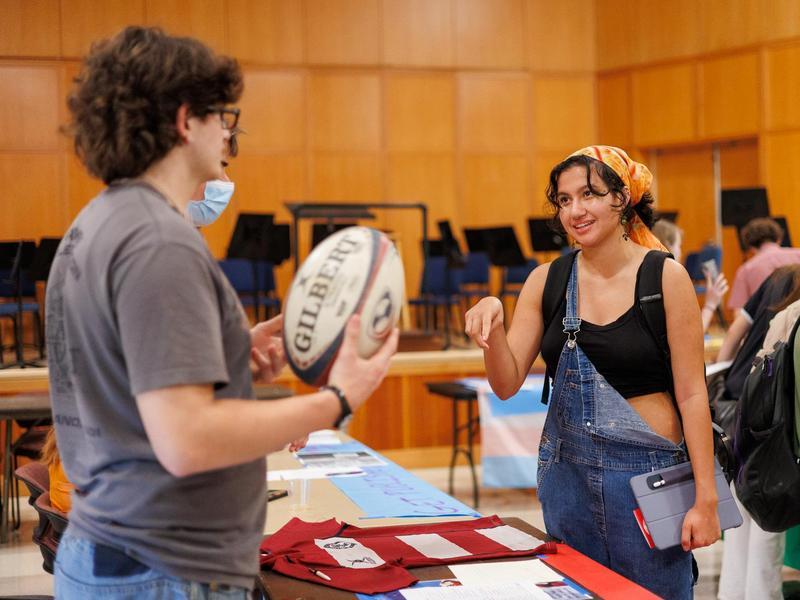 A student learns about the Rugby Club from a club member holding a rugby ball during the student clubs fair.