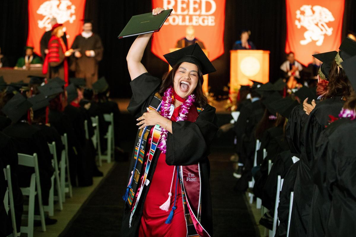 A graduate raises her diploma in the air in celebration while walking down the aisle during commencement.
