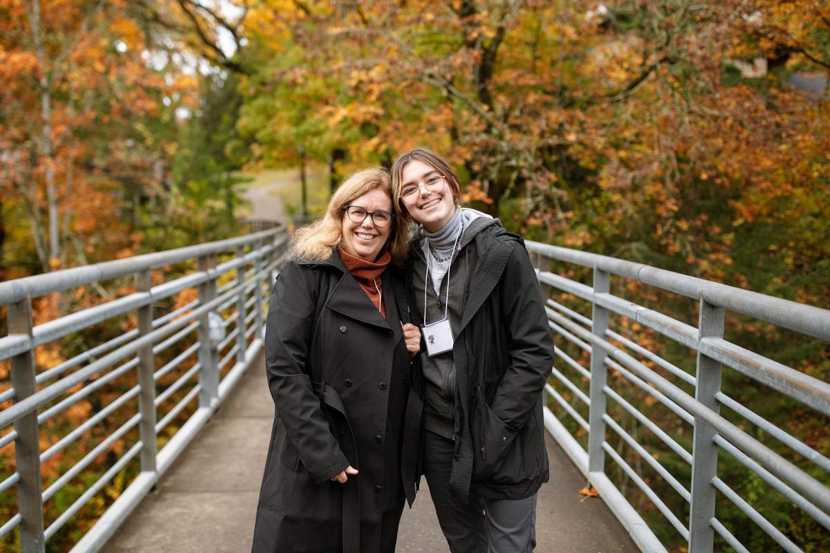A student and parent pose and smile on the Blue Bridge over Reed canyon during Parents and Family Weekend.