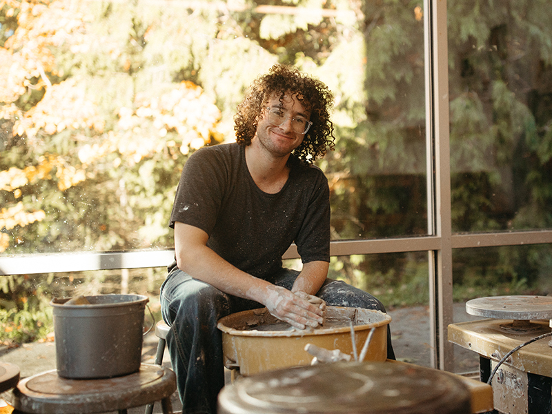 A student smiles while working at a pottery wheel.