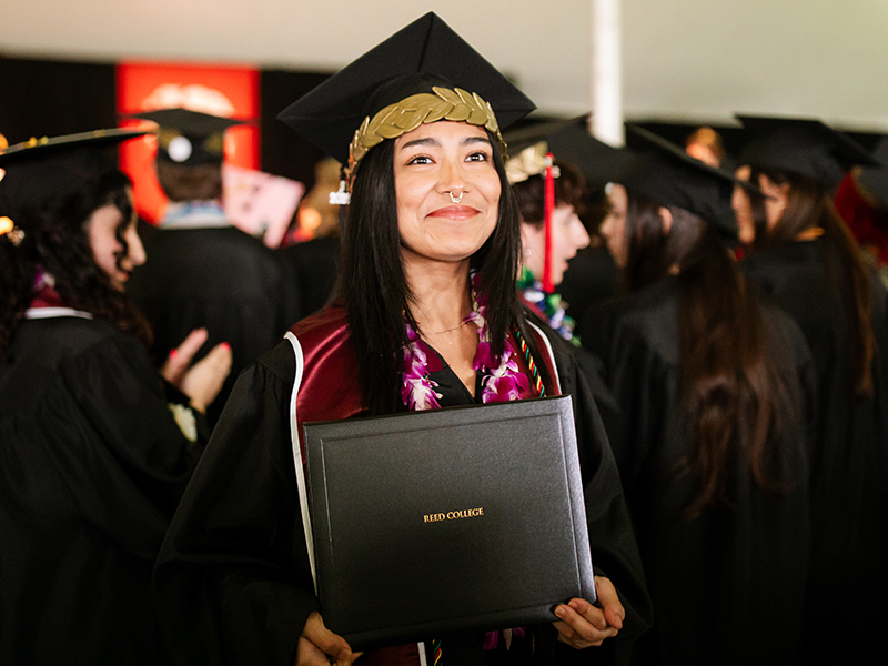 A graduate in regalia holds a diploma during Commencement.
