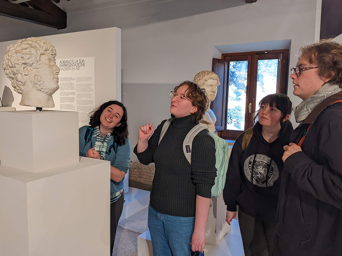 Four students look at a bust of a Roman historical figure in a museum gallery.