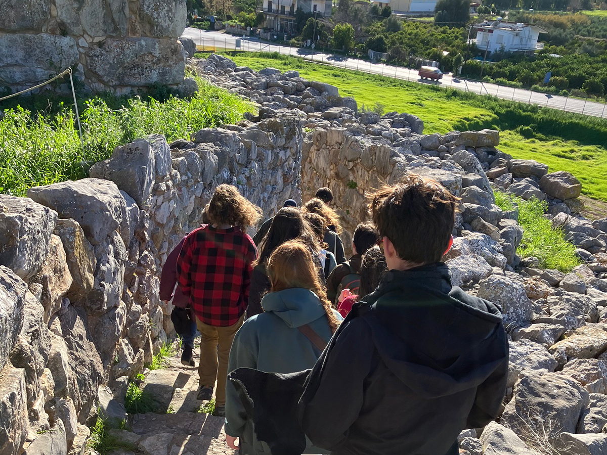 A group of students walk down a stone staircase at a Greek archaeological site.