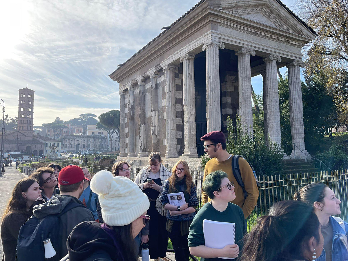 A group of students on a walking tour among ancient Roman architecture.