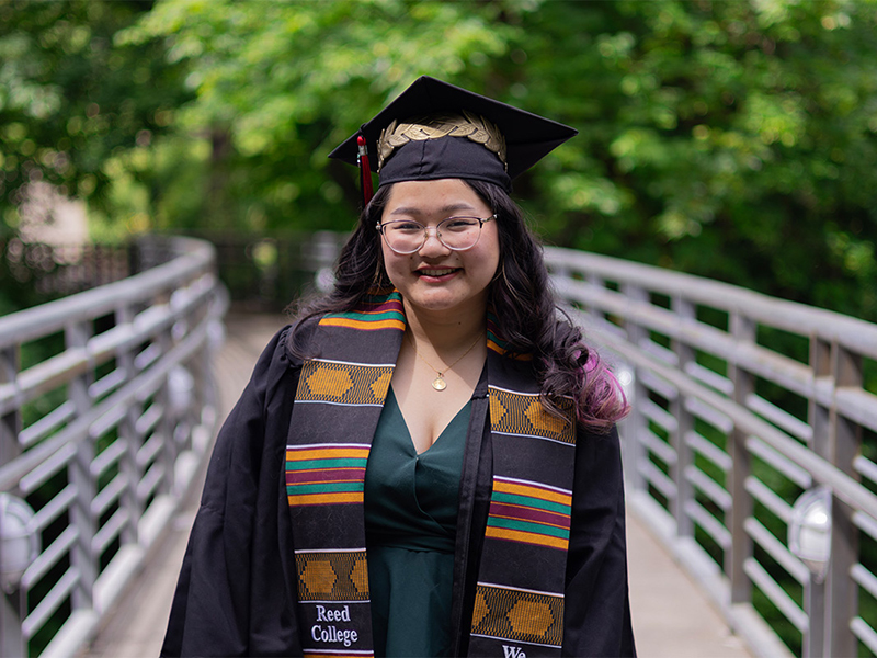 Sydney Stitt poses for a photo on the Blue Bridge while wearing graduation regalia.