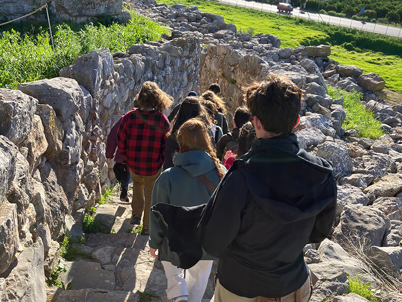 A group of students walk down a stone staircase at a Greek archaeological site.