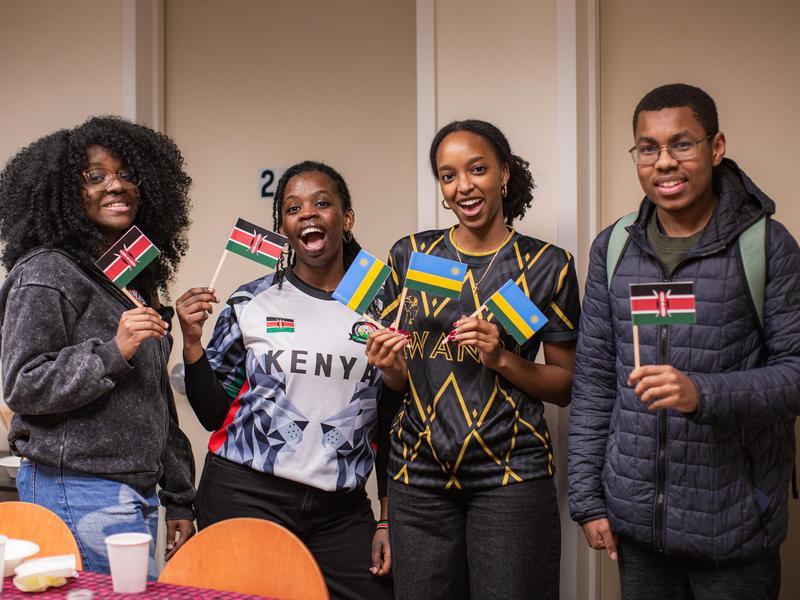 Four students pose while holding small Kenyan and Rwadan flags.