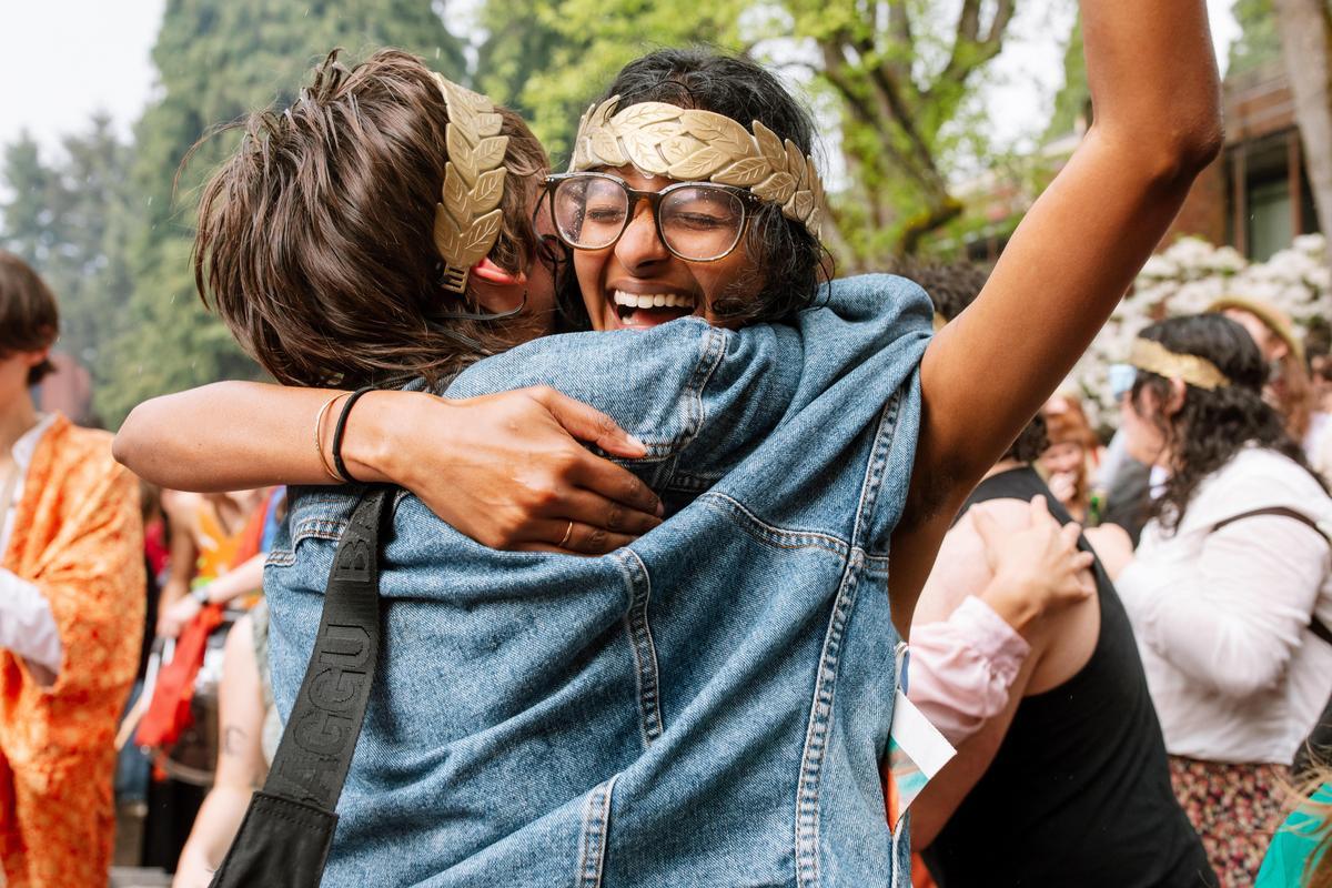 Two students wearing gold laurels hugging during the thesis celebration.