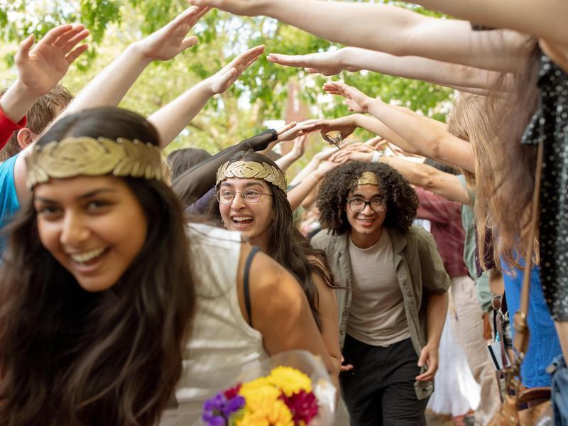 A line of graduating students wearing laurels walk under a human tunnel during Renn Fayre.