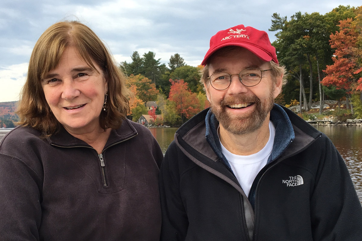 Mary Bandura and Harton Smith sitting outside surrounded by autumnal trees and a body of water.