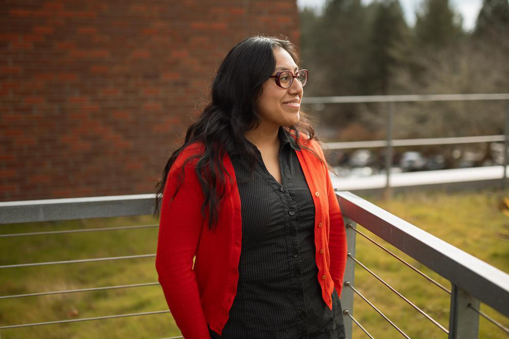 Flor Lopez smiling and looking into the distance while standing on a rooftop patio.