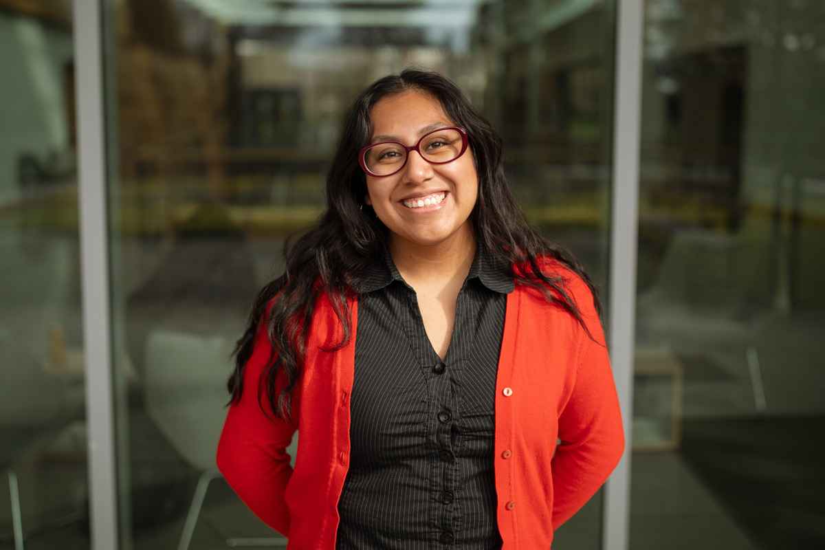 Headshot of Flor Lopez standing in front of a large glass window.