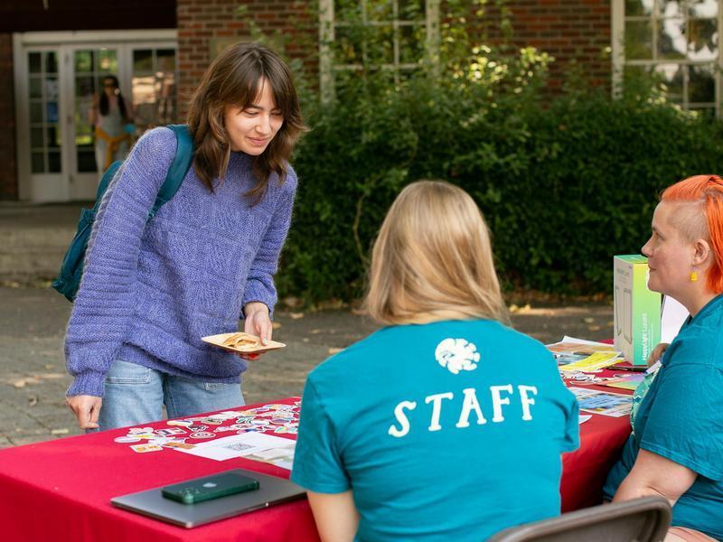 A student browses a resource table hosted by two college staff members.