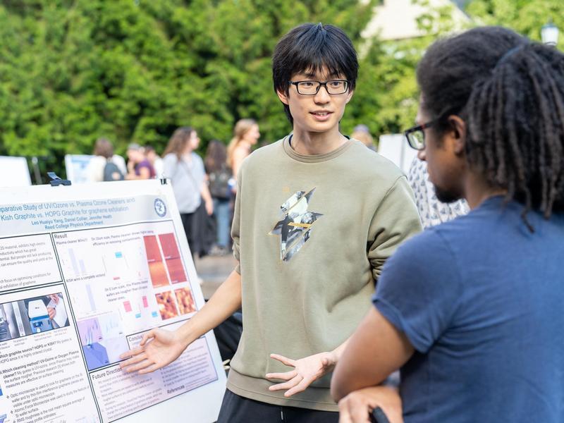 A student presents a research poster to an event attendee.