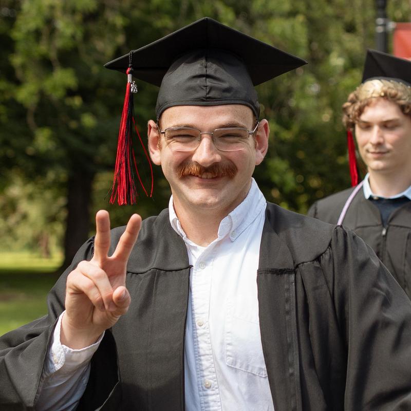 Oscar Pulliam wearing graduation regalia and posing with a peace sign.
