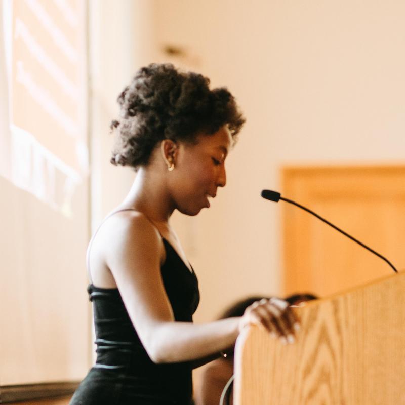 Side profile of Whitney Kuma-Perry speaking at a lectern.